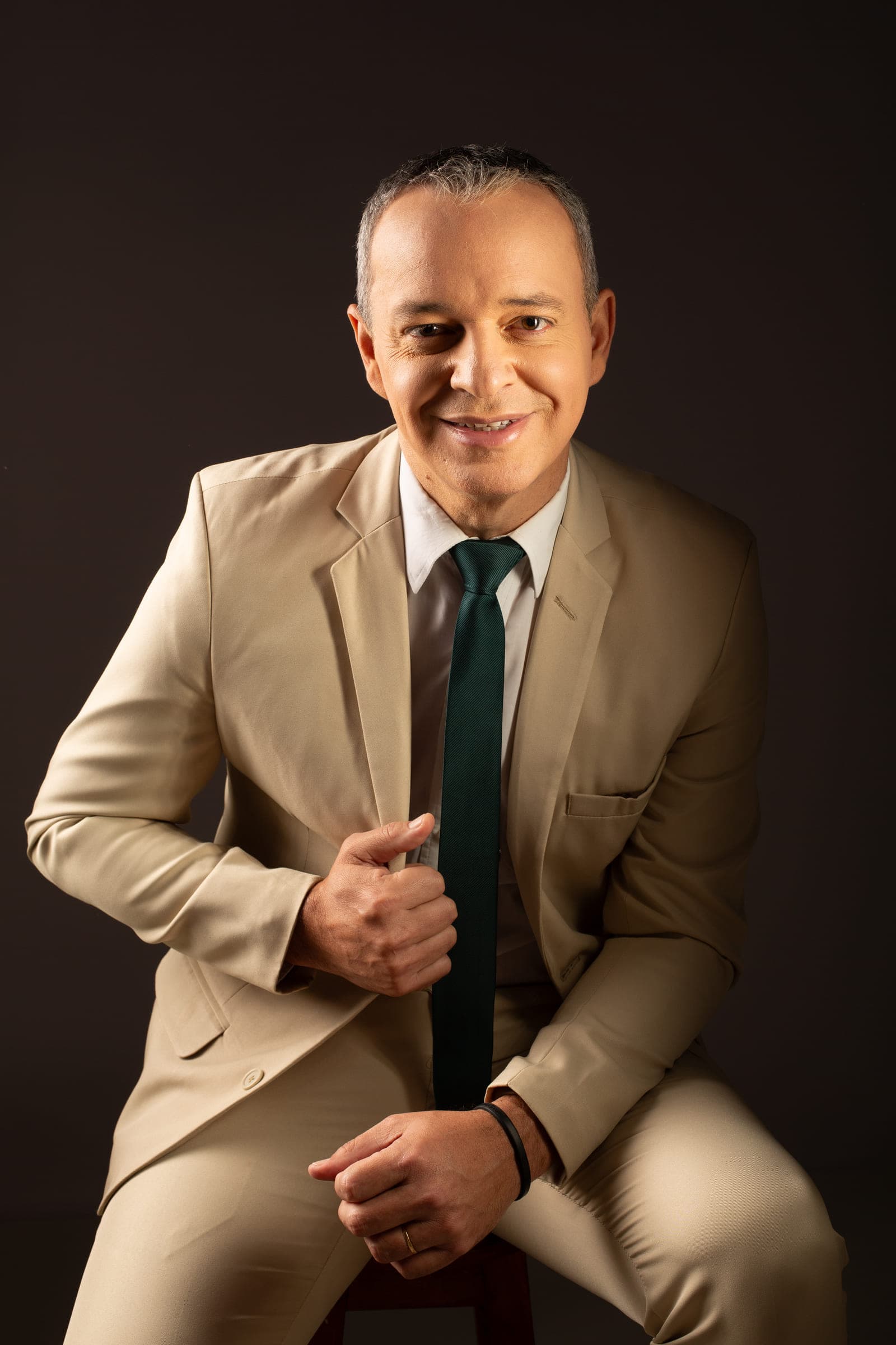 Paulo Crispim em retrato de estúdio, sentado, de terno claro e gravata verde